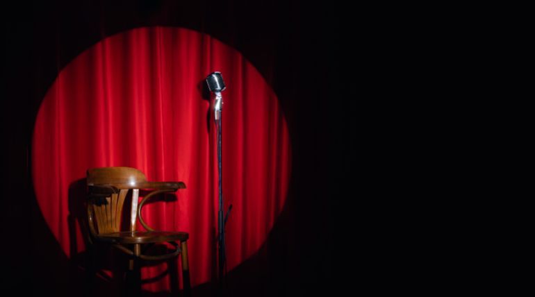Concept banner standup comedian show. Old microphone and armchair on theater stage on red curtains background.