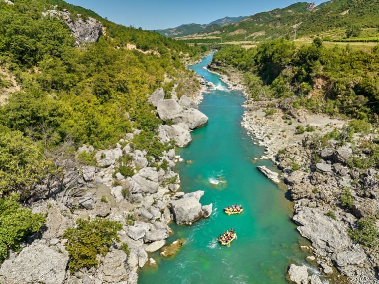 Cooperation concept: Adventure and sport. Two yellow rafts floating among the rocks on the crystal clear, blue-green water. Perpendicular drone view of the rafters floating on Vjose river, Albania.