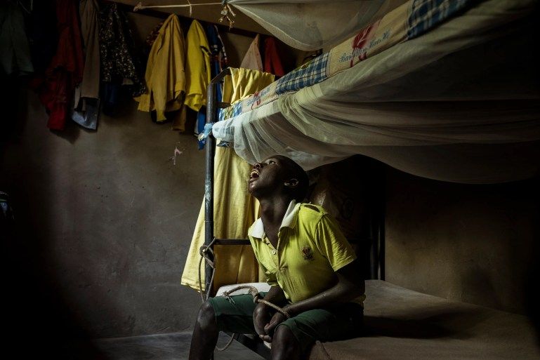 In Omalera, 17-year-old David Emwodu sits with his hands bound by a rope tied to the bunk bed he shares with his brother. David lives with an undiagnosed intellectual disability. He can become violent, especially towards his eldest brother, and when this occurs, his family tethers him to the bed [Christopher Hopkins/Al Jazeera]