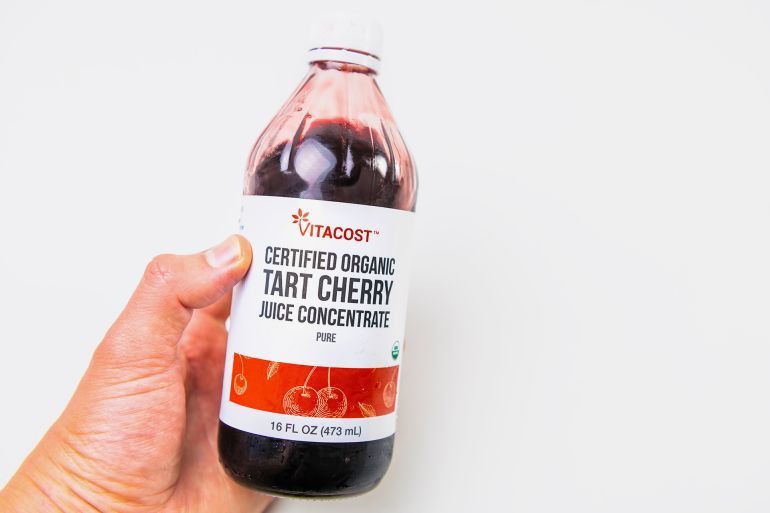 Naples, USA - October 21, 2021: Hand holding closeup of glass drink bottle of tart organic cherry juice concentrate by Kroger Vitacost brand; Shutterstock ID 2219987389; purchase_order: aj; job: ; client: ; other: