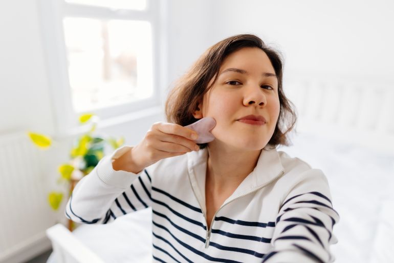 Woman vlogging and doing face massage with a guasha scraper
