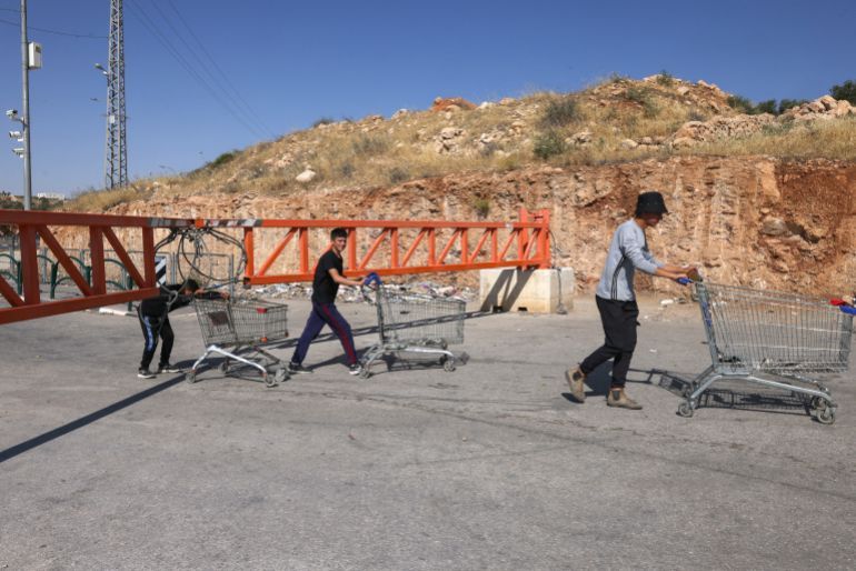 Palestinian boys push shopping carts as people move on foot across closed iron gate set up by Israeli forces after Israeli authorities closed off all entrance and exist roads of Hebron city in the occupied West Bank on June 14, 2025. (Photo by HAZEM BADER / AFP)
