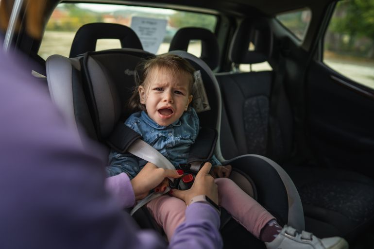 One woman unknown mother putting girl small caucasian toddler female child sitting in the safety car seat chair 18 months old cry protest negative emotion transportation concept copy space