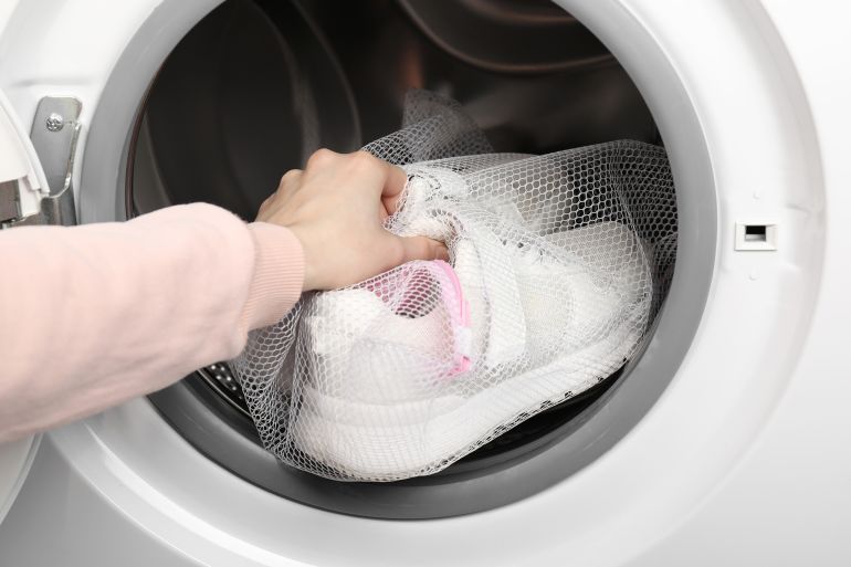 Woman putting stylish sneakers into washing machine, closeup